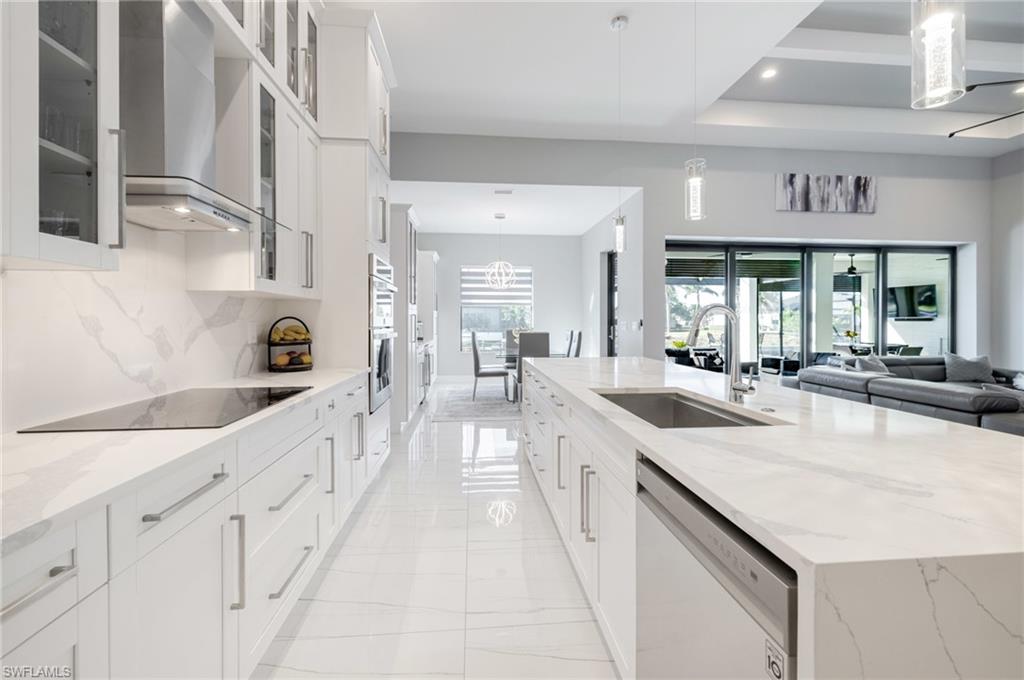 Kitchen featuring white cabinetry, light stone counters, stainless steel appliances, glass fronted cabinets, and a tray ceiling