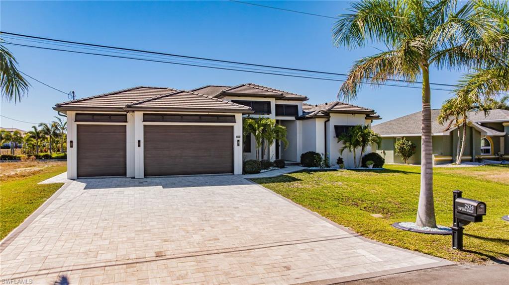 View of front of house with a front yard, decorative driveway, stucco siding, an attached garage, and a tile roof