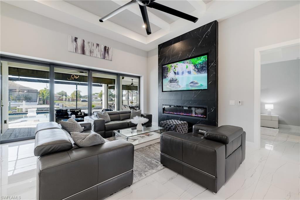 Living area with ceiling fan, light marble finish floors, coffered ceiling, and a high end fireplace