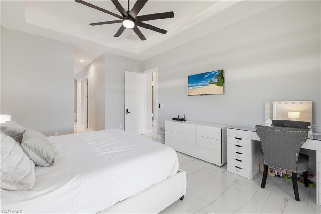Bedroom with an office area, ceiling fan, light marble finish floors, a raised ceiling, and recessed lighting