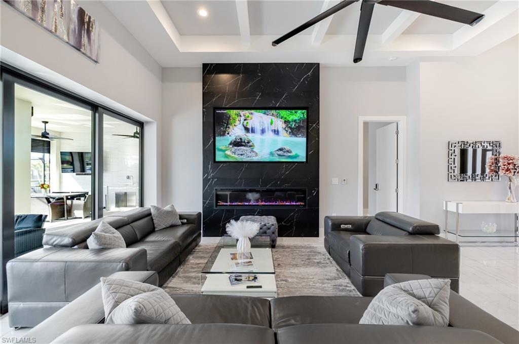 Living room with a ceiling fan, beam ceiling, a premium fireplace, an accent wall, and recessed lighting