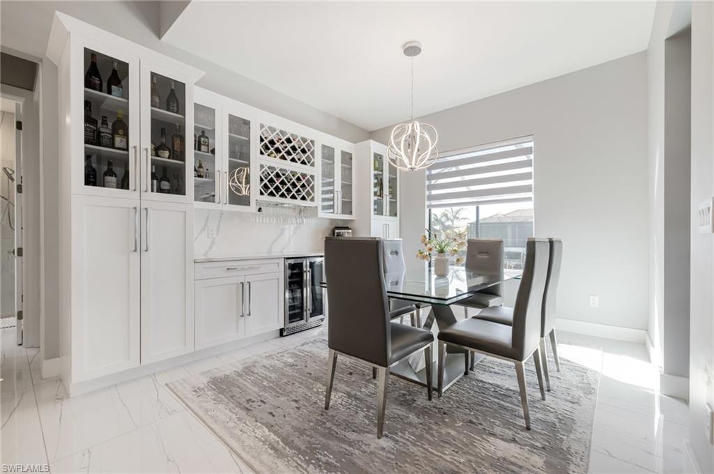 Dining area featuring beverage cooler, hanging lights, light marble finish flooring, and a dry bar
