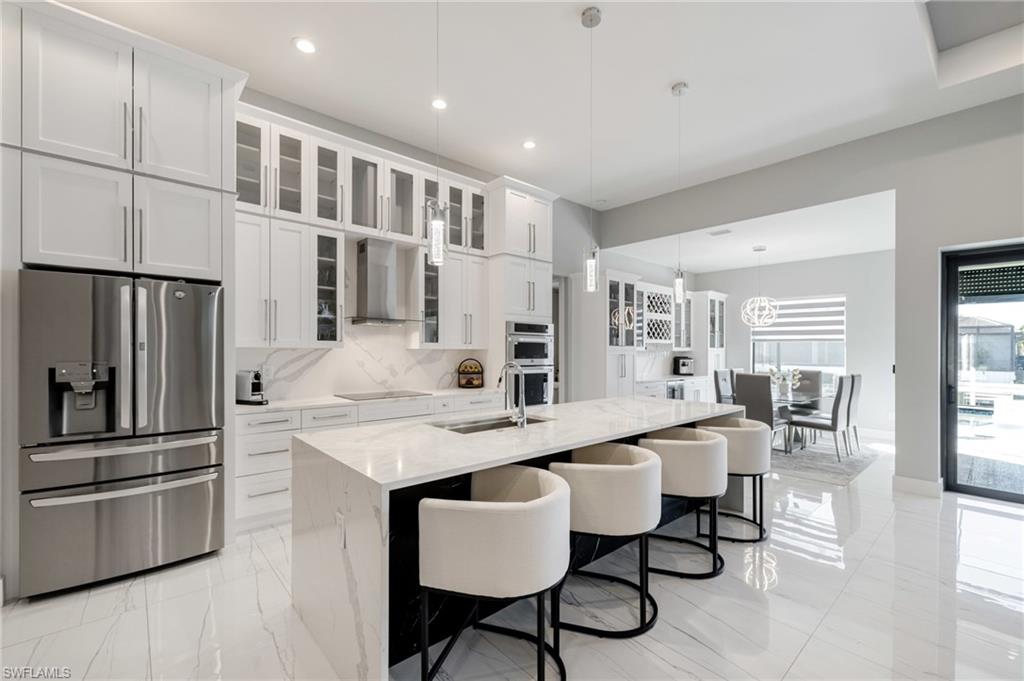 Kitchen featuring stainless steel appliances, glass fronted cabinets, light stone countertops, a kitchen island with sink, and white cabinetry