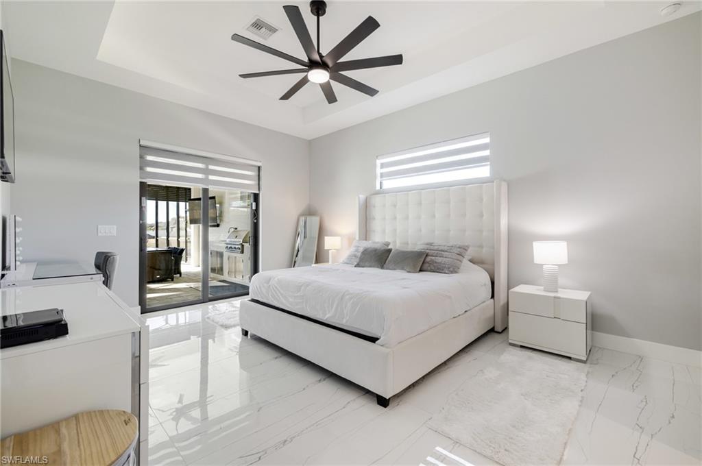 Bedroom with light marble finish floors, a ceiling fan, access to exterior, and a raised ceiling