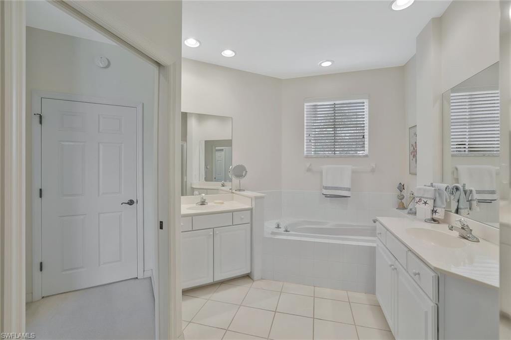 Bathroom featuring two vanities, light tile patterned floors, a garden tub, and recessed lighting