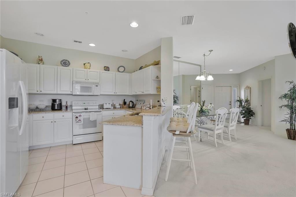Kitchen with white appliances, white cabinets, a kitchen bar, light stone counters, and a peninsula