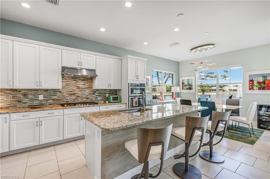 Kitchen featuring light stone counters, white cabinets, a kitchen island with sink, recessed lighting, and a kitchen breakfast bar
