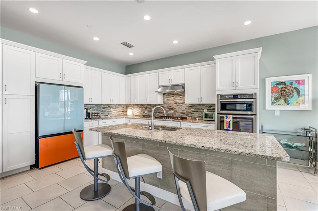 Kitchen with light stone counters, stainless steel appliances, white cabinets, a breakfast bar, and tasteful backsplash