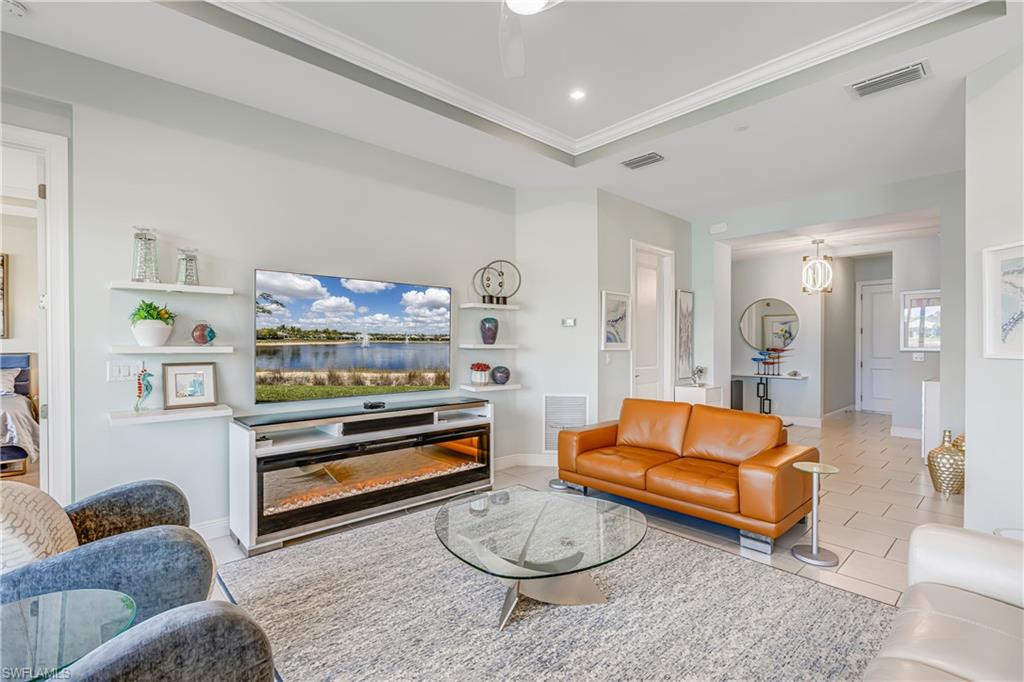 Living room with light tile patterned floors, crown molding, a ceiling fan, and a raised ceiling