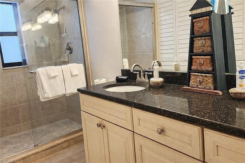 Dual-sink vanity adorned with a polished granite countertop, complemented by a beautifully appointed, glass-enclosed walk-in tiled shower for a spa-inspired retreat.