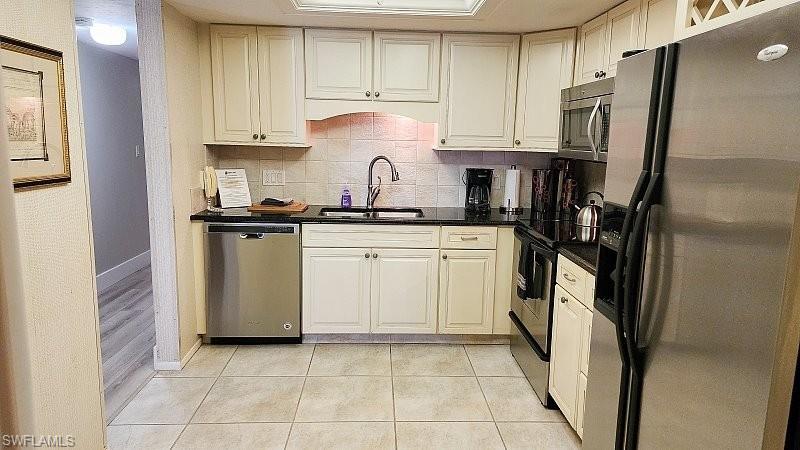 Kitchen with stainless steel appliances, decorative backsplash, white cabinetry, dark stone counters, and light tile patterned floors