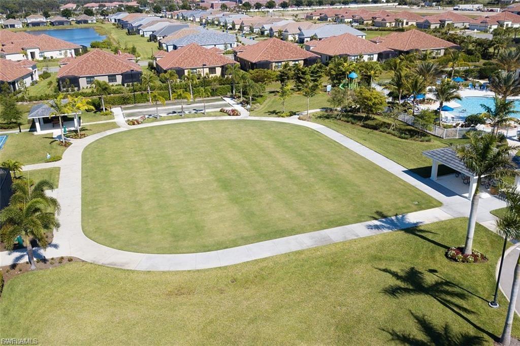 Expansive green lawn surrounded by a paved pathway, featuring mature palm trees and landscaped grounds