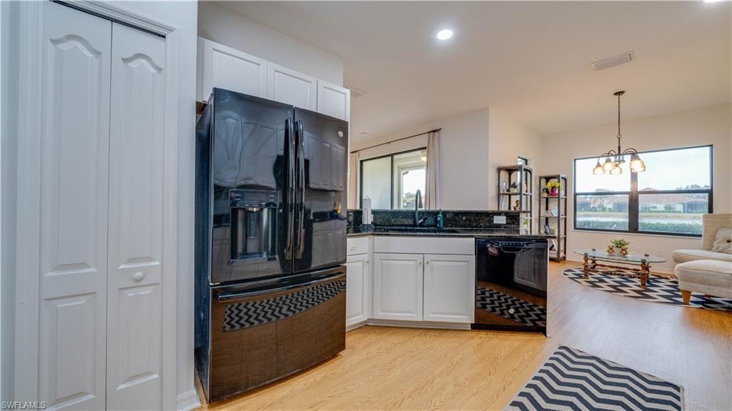 Kitchen with black appliances, hanging lights, white cabinetry, light wood-type flooring, and a peninsula