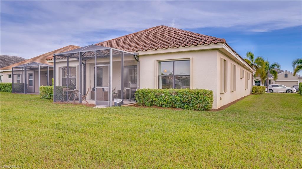 Rear view of house with stucco siding, a lanai, a yard, a tile roof, and a sunroom