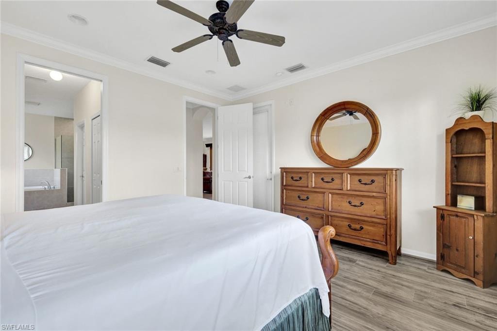 Bedroom featuring ornamental molding, light wood-style floors, a ceiling fan, and ensuite bath