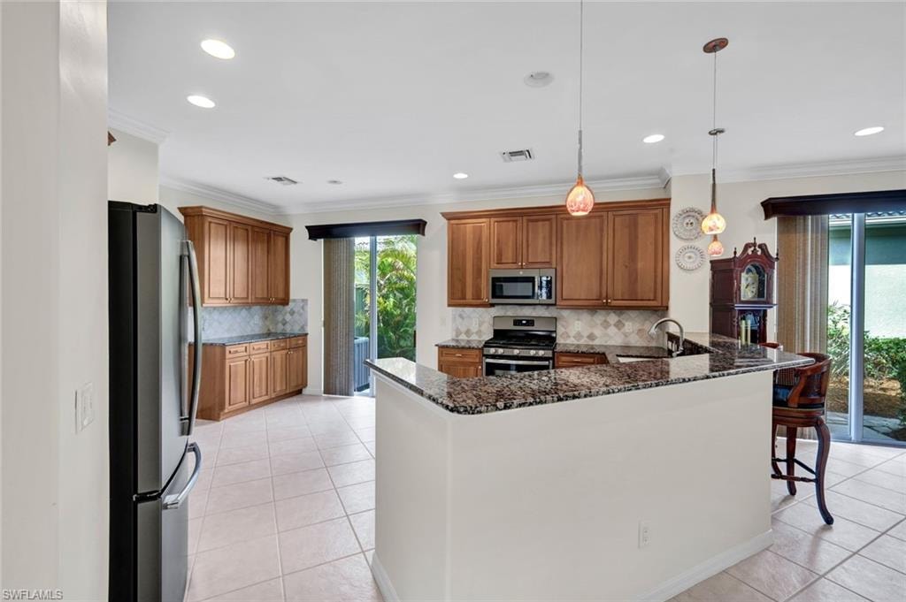 Kitchen with wood finish cabinetry, a peninsula, stainless steel appliances, dark stone countertops, and light tile patterned floors