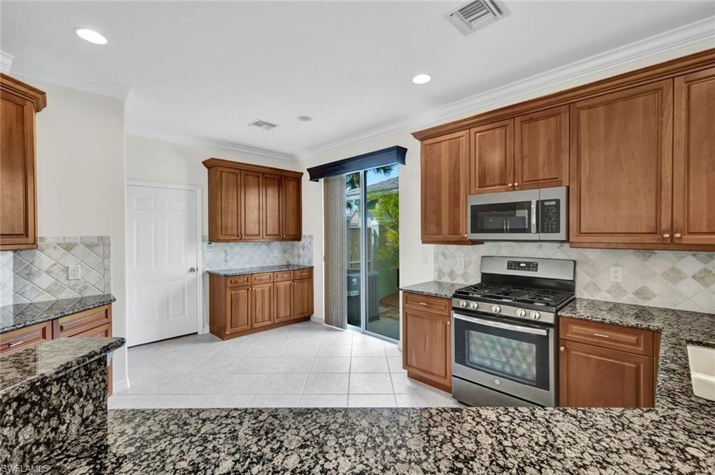 Kitchen featuring stainless steel appliances, dark stone counters, backsplash, wood finish cabinets, and crown molding