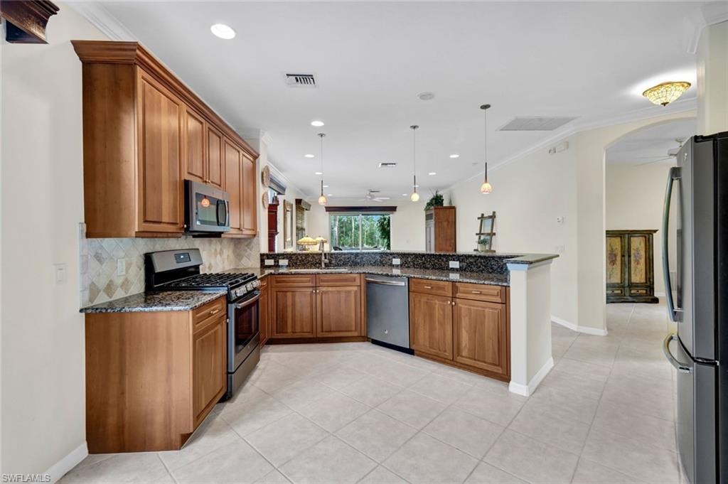 Kitchen with wood finish cabinetry, stainless steel appliances, dark stone counters, pendant lighting, and light tile patterned floors