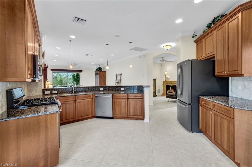 Kitchen with tasteful backsplash, wood finish cabinets, dark stone counters, decorative light fixtures, and ceiling fan