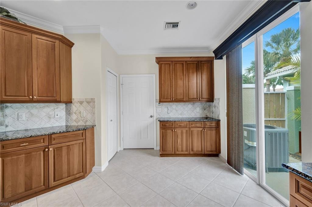 Kitchen featuring wood finish cabinetry, dark stone counters, light tile patterned flooring, and crown molding