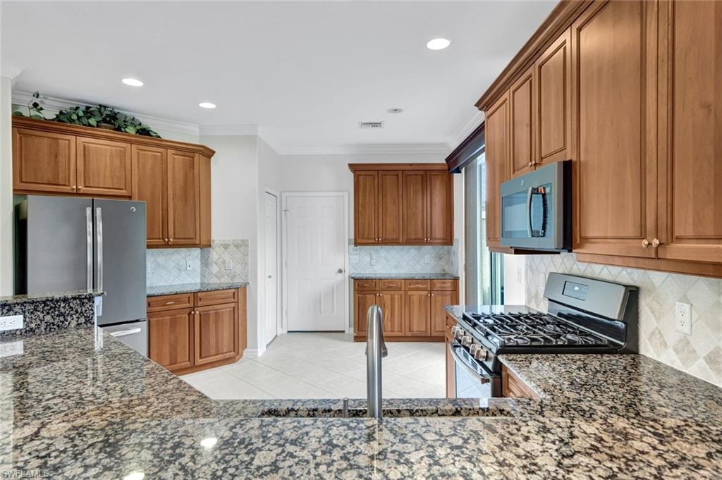 Kitchen with stainless steel appliances, wood finish cabinetry, crown molding, light tile patterned flooring, and dark stone countertops
