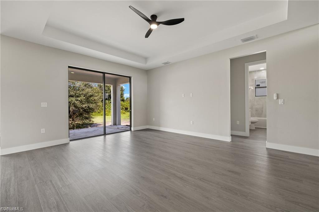 Empty room with a tray ceiling, a ceiling fan, and dark wood-style flooring