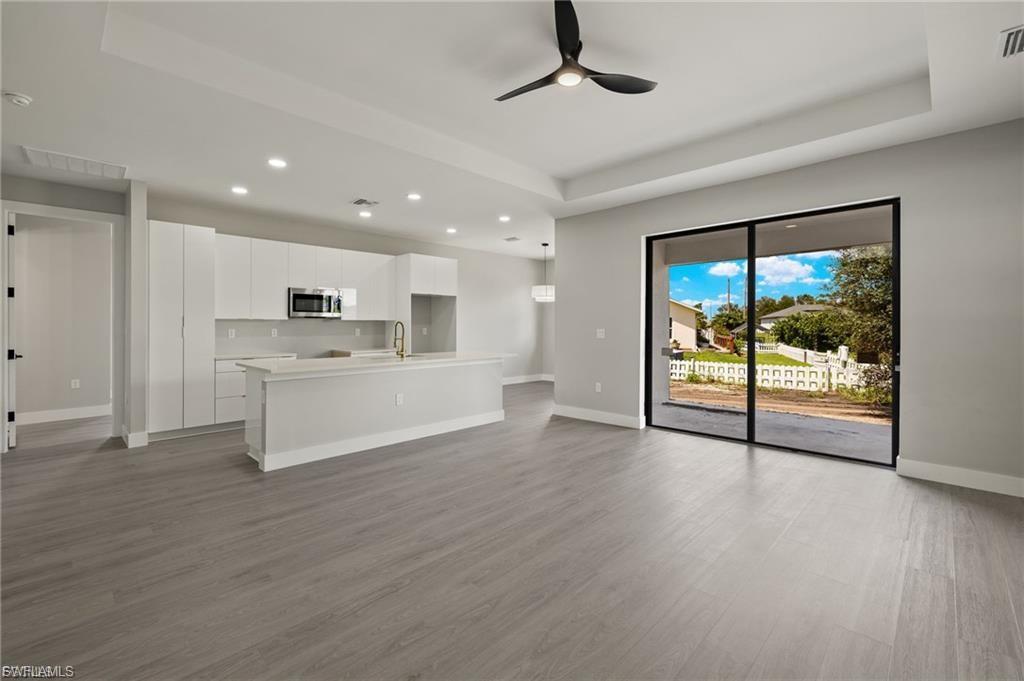 Unfurnished living room with a tray ceiling, ceiling fan, dark wood-style floors, and recessed lighting