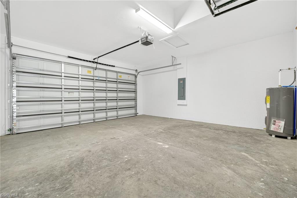 Garage with electric water heater, electric panel, and a garage door opener