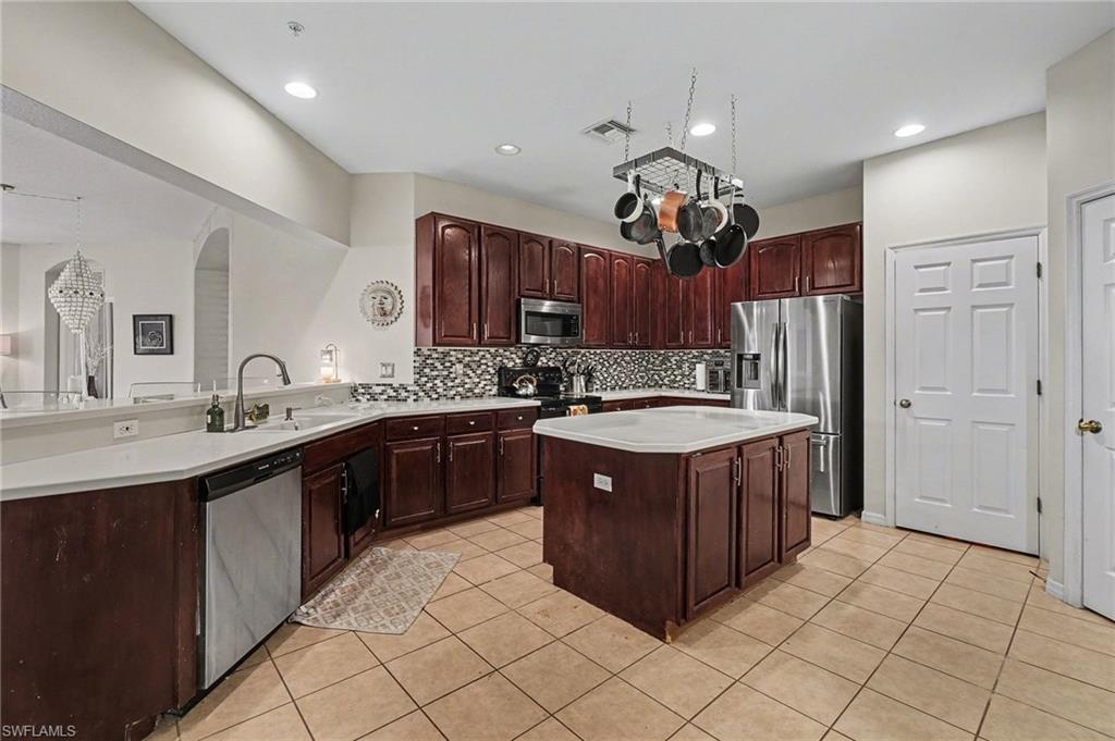 Kitchen featuring stainless steel appliances, light countertops, a center island, light tile patterned flooring, and a peninsula