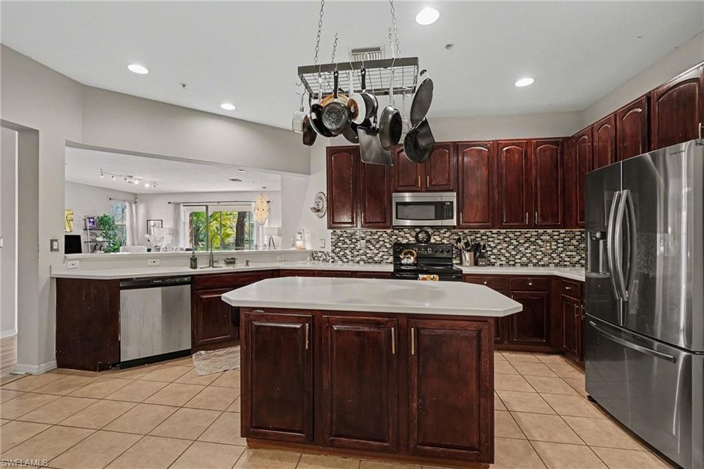Kitchen featuring stainless steel appliances, a center island, light countertops, light tile patterned flooring, and decorative backsplash