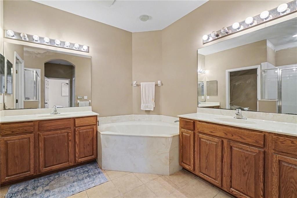 Primary Bathroom with two vanities, a garden tub, a shower stall, and light tile patterned flooring
