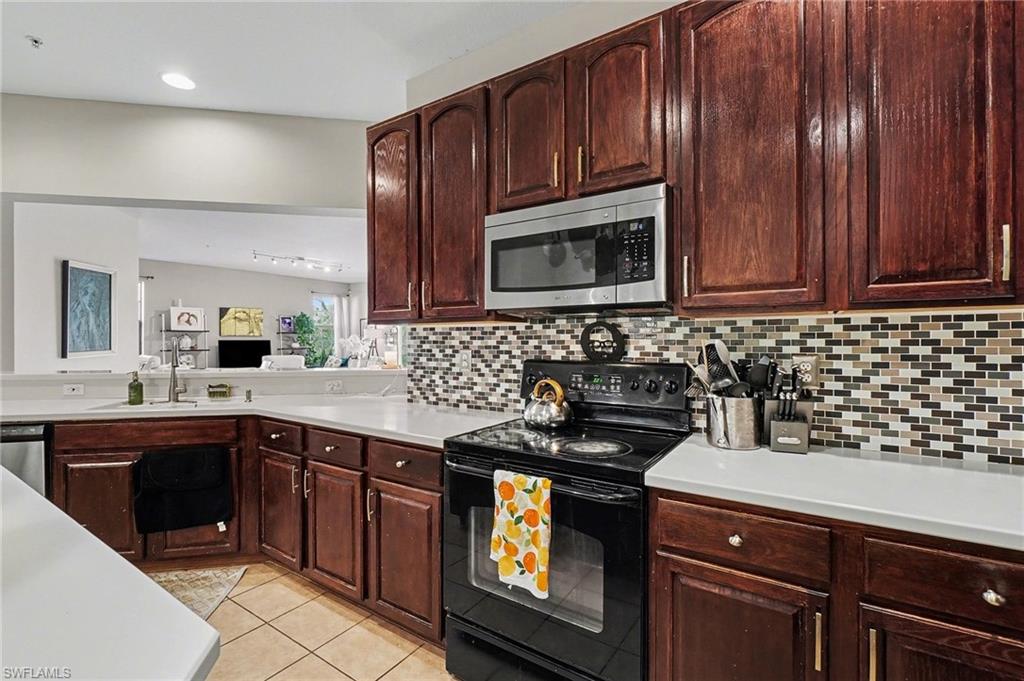 Kitchen with black electric range, stainless steel microwave, light countertops, light tile patterned flooring, and backsplash