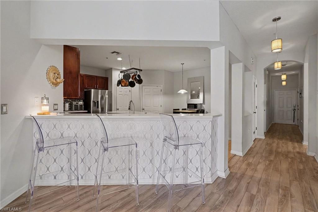 Kitchen with light wood-style floors, stainless steel fridge, hanging light fixtures, arched walkways, and a breakfast bar