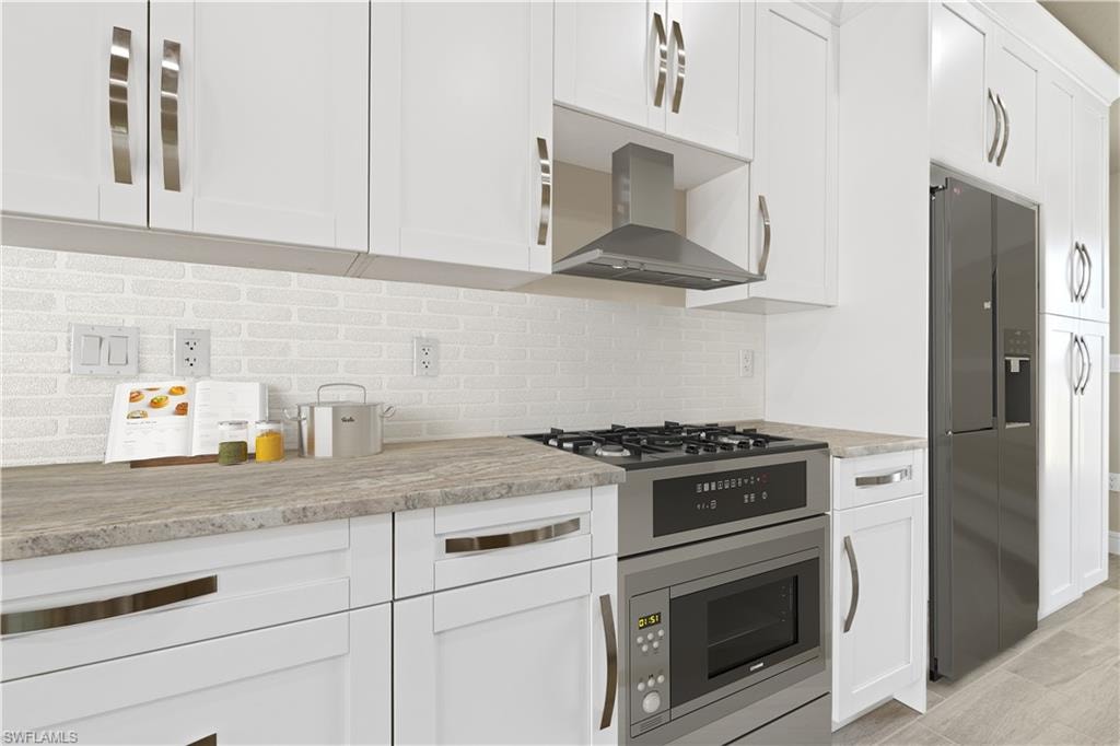 Kitchen with white cabinetry, fridge with ice dispenser, backsplash, light stone counters, and stainless steel microwave