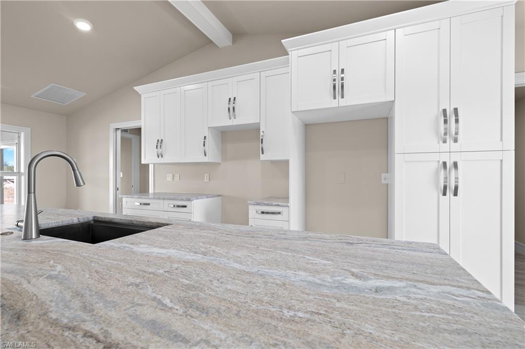 Kitchen featuring white cabinets, light stone counters, beamed ceiling, and recessed lighting