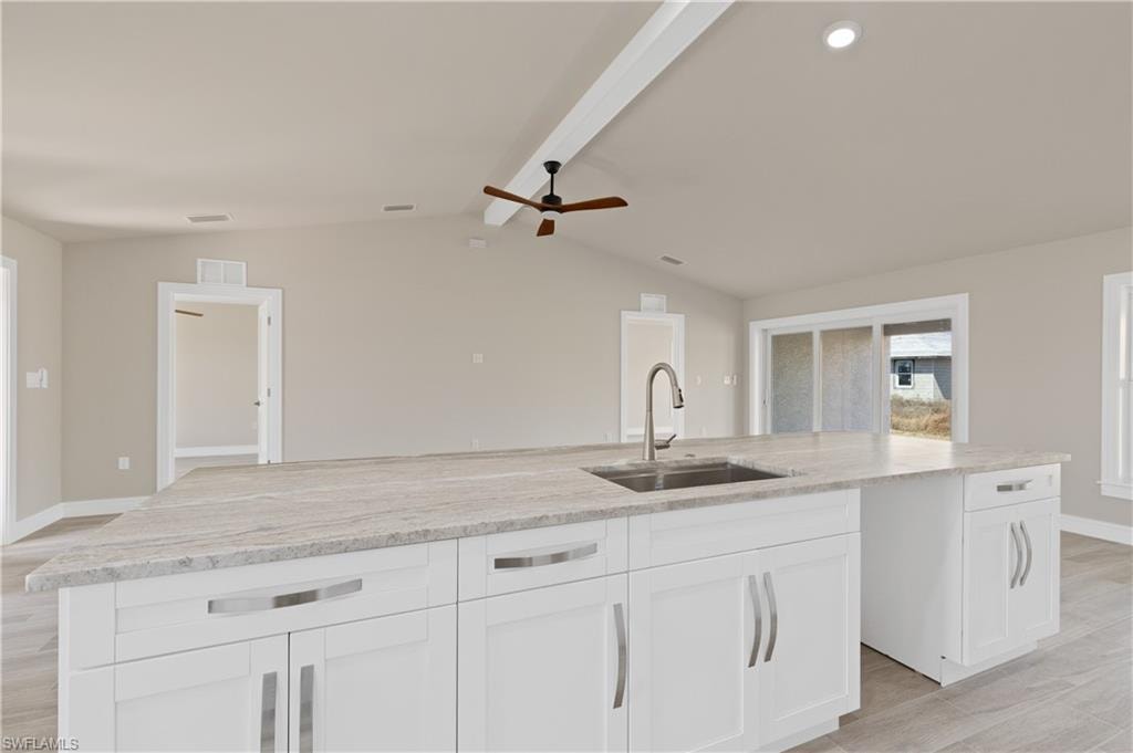 Kitchen with a ceiling fan, light stone countertops, a kitchen island with sink, light wood-type flooring, and white cabinets