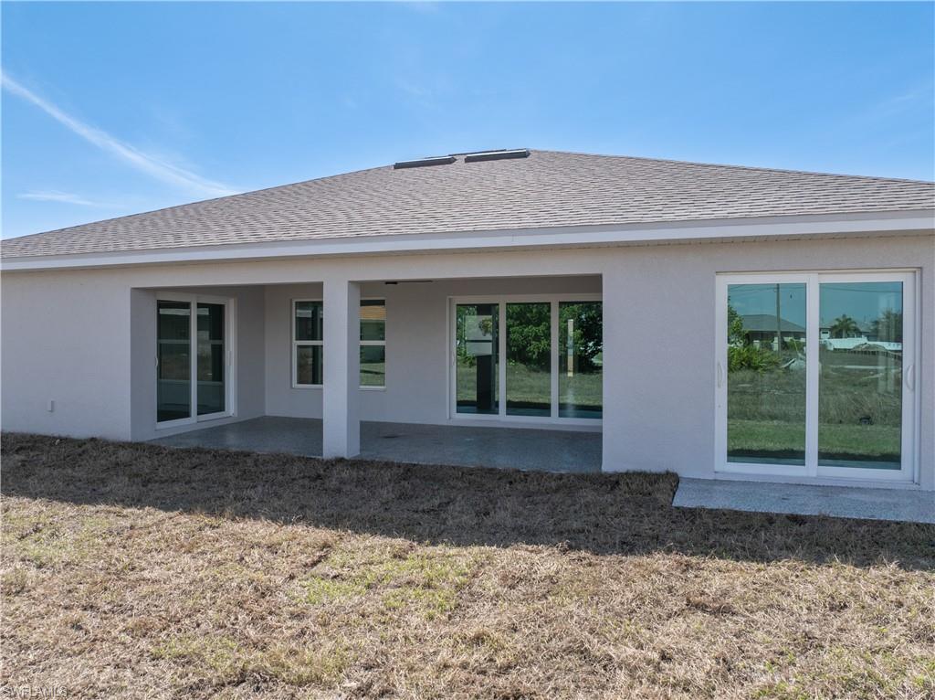 Rear view of property with a patio area, stucco siding, a shingled roof, and a lawn