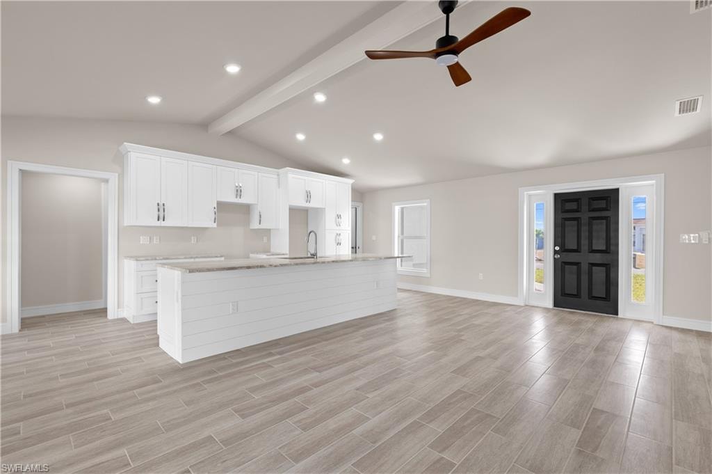 Kitchen featuring white cabinetry, a center island with sink, a ceiling fan, wood tiled floors, and light stone counters