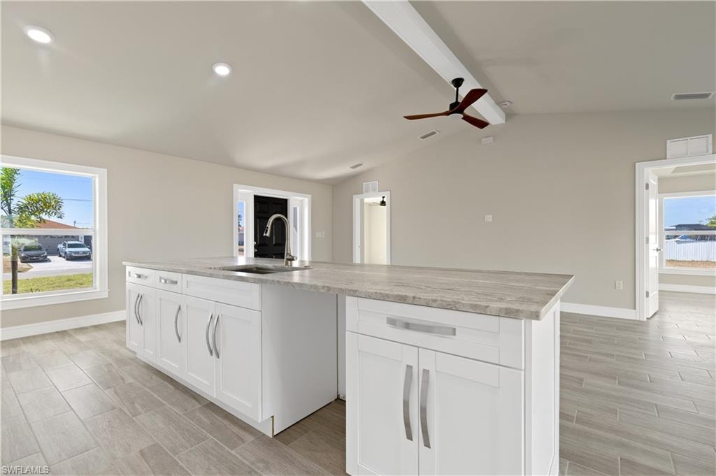 Kitchen featuring white cabinets, a ceiling fan, an island with sink, wood tiled floors, and light stone counters