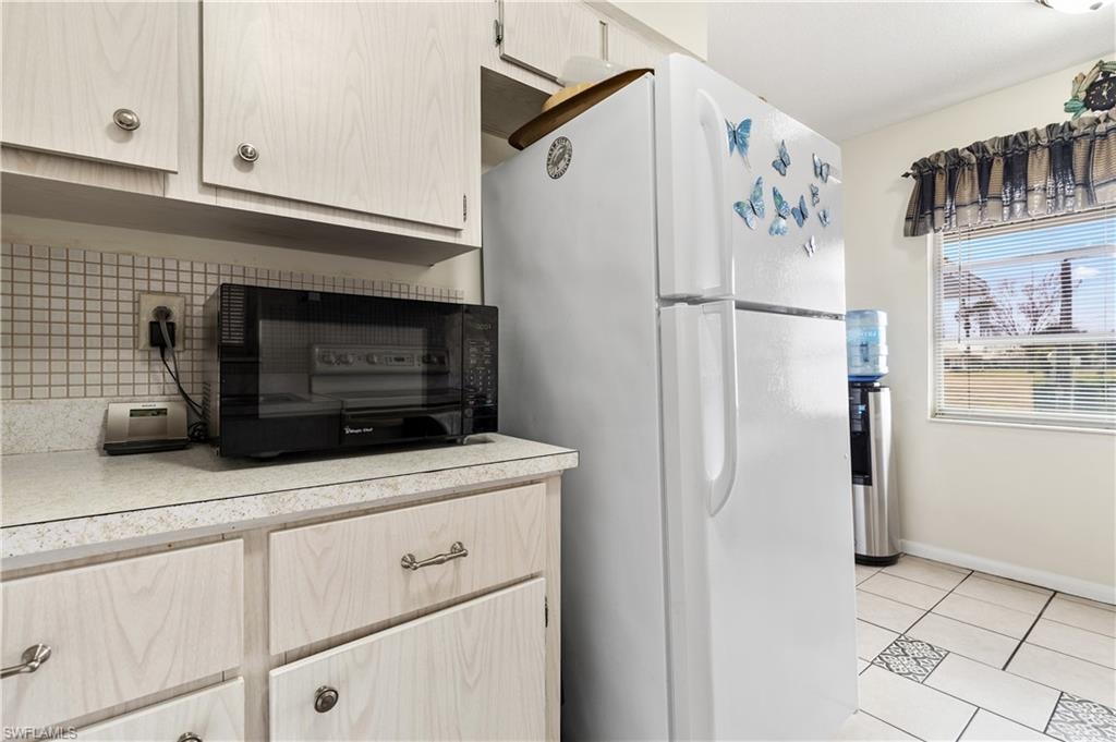 Kitchen with freestanding refrigerator, light countertops, black microwave, light tile patterned floors, and decorative backsplash