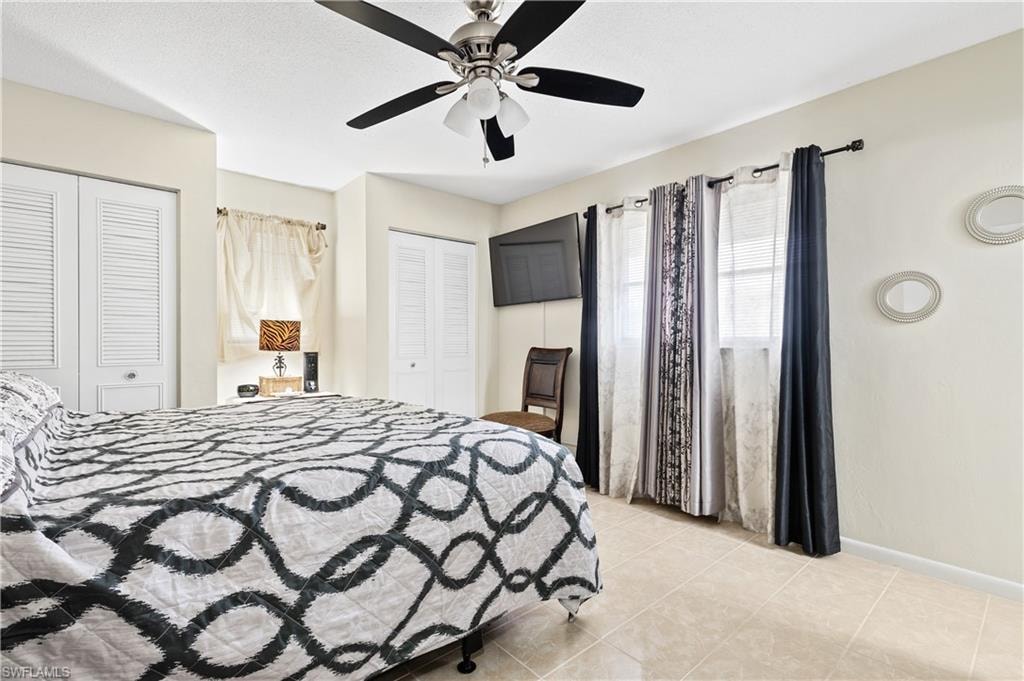 Bedroom with two closets, ceiling fan, and light tile patterned floors