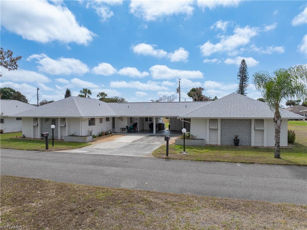 Ranch-style house with a carport, a front yard, a shingled roof, and driveway