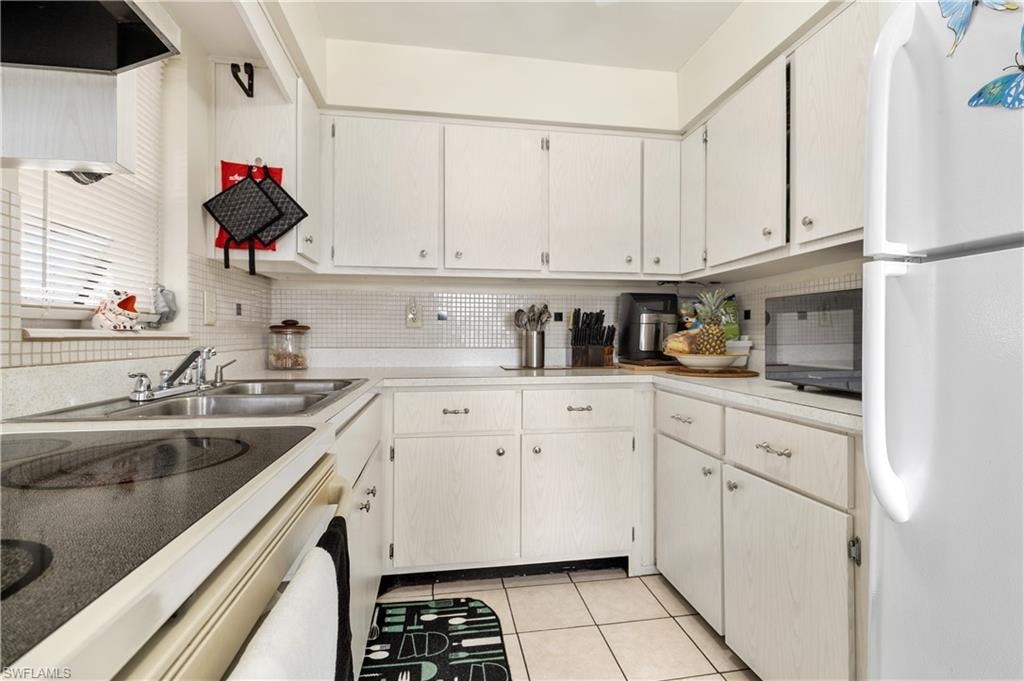 Kitchen with freestanding refrigerator, light countertops, black microwave, light tile patterned flooring, and electric range oven