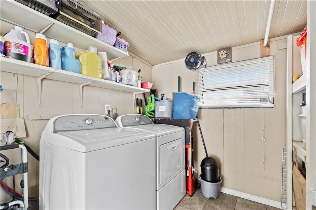 Laundry room with separate washer and dryer, wooden walls, and light tile patterned floors