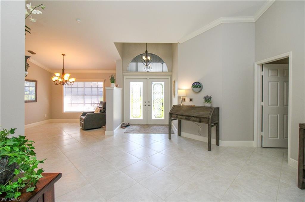 Entryway featuring light tile patterned floors, baseboards, an inviting chandelier, and crown molding