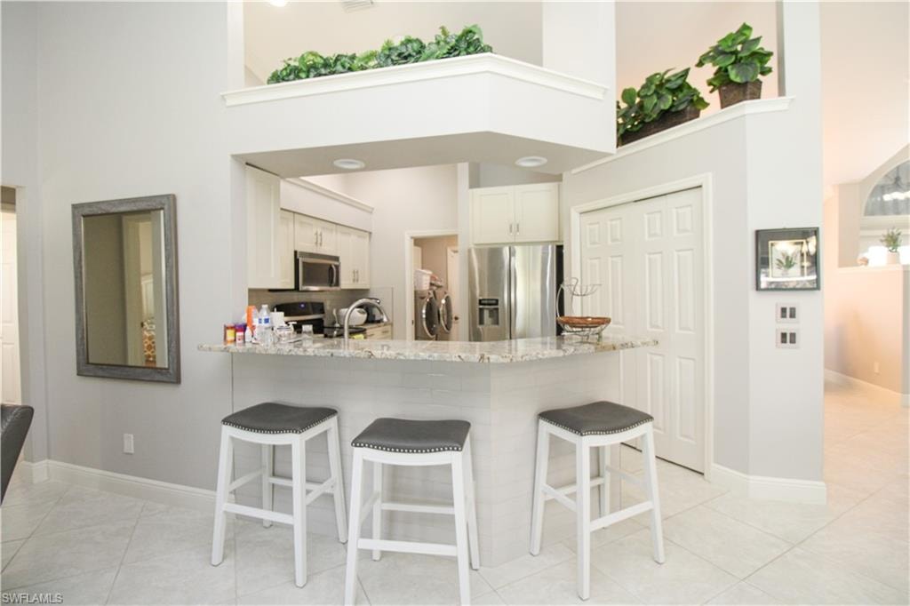 Kitchen featuring light stone countertops, a kitchen bar, a peninsula, a high ceiling, and stainless steel appliances