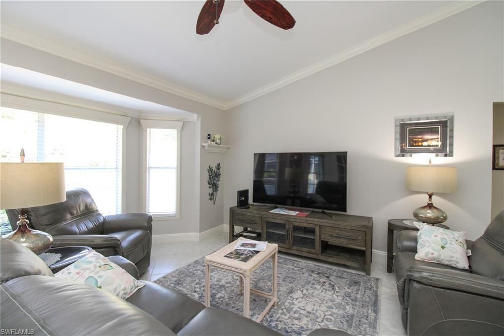 Tiled living room featuring vaulted ceiling, ornamental molding, baseboards, and ceiling fan