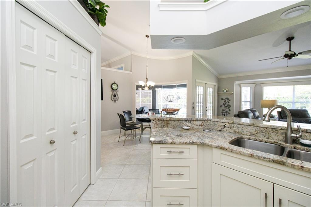 Kitchen with light tile patterned floors, ornamental molding, a sink, vaulted ceiling, and ceiling fan with notable chandelier