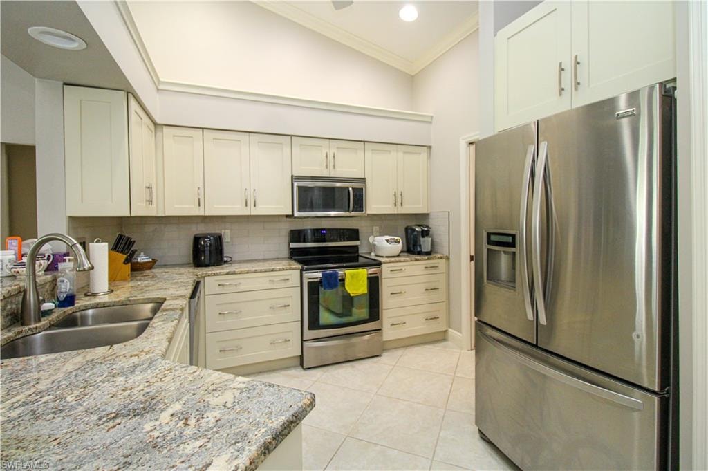 Kitchen with light tile patterned flooring, a sink, decorative backsplash, ornamental molding, and stainless steel appliances