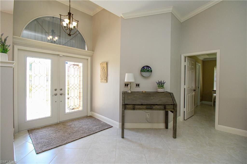 Foyer with french doors, a notable chandelier, a towering ceiling, and crown molding